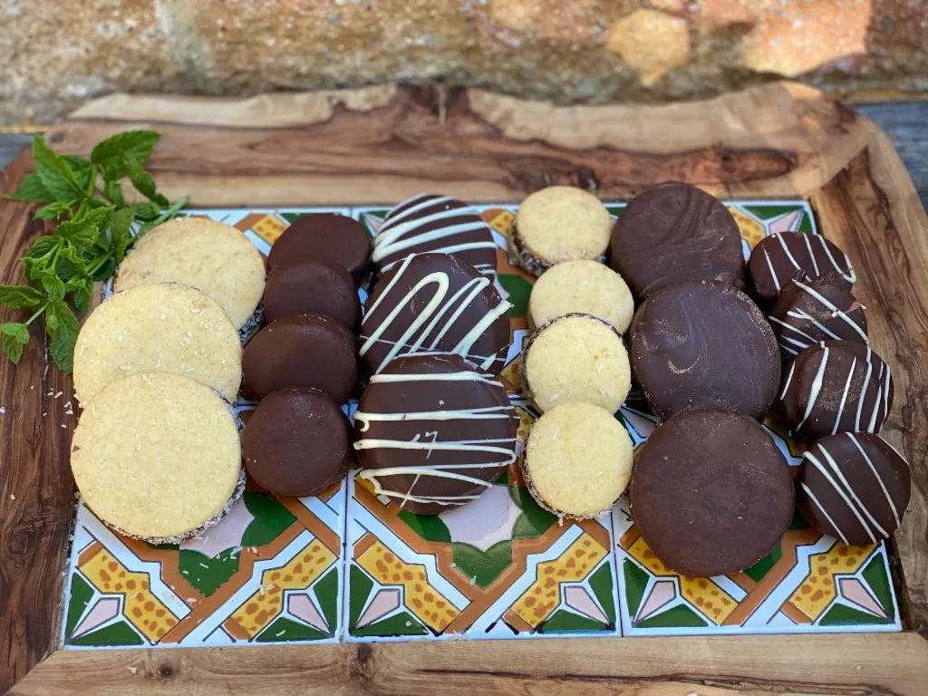 Verschiedene Alfajores auf Holzbrett – mit Kokos, Schokolade und weißer Glasur, aus Diegos Genusswerkstatt