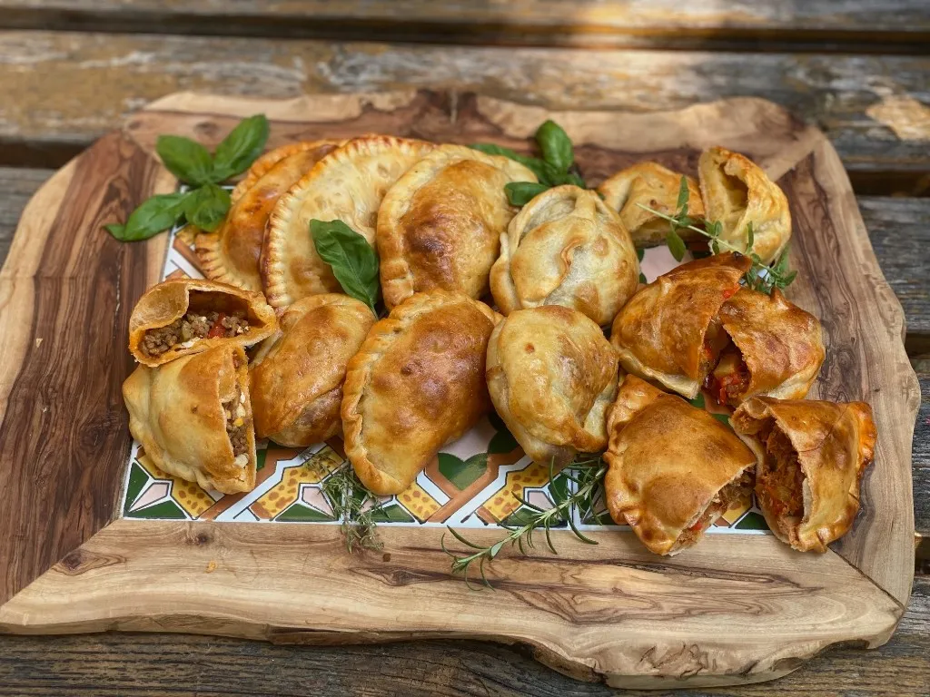 Verschiedene Empanadas auf Holzbrett, einige im Schnitt – frisch aus Diegos Genusswerkstatt